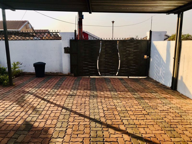 A covered carport area featuring a paved driveway and a secure metal gate entrance.