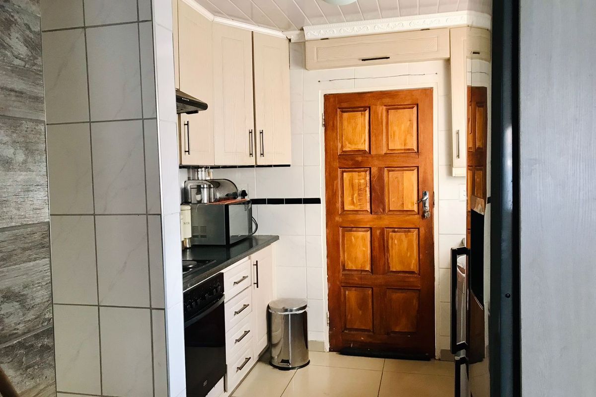 A functional kitchen featuring built-in cabinetry, a tiled splashback, and a timber door, offering a practical layout with standard fixed finishes.
