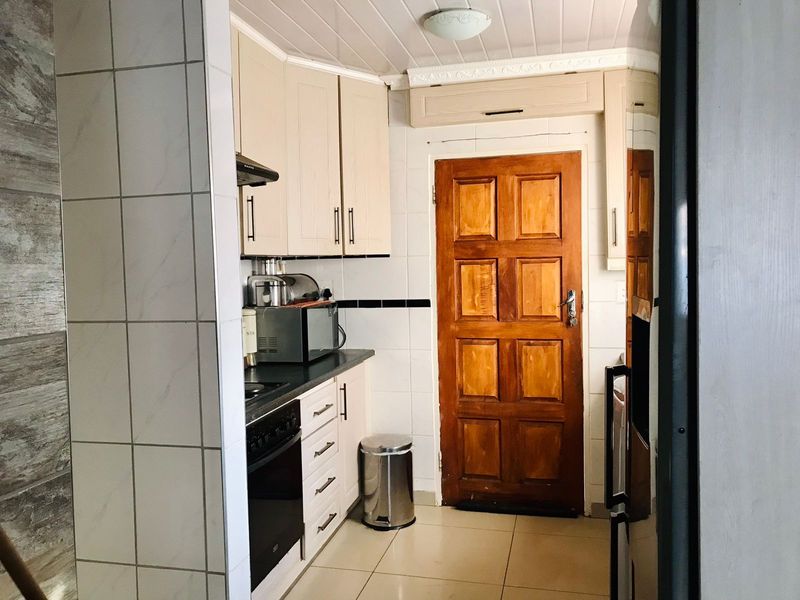 A functional kitchen featuring built-in cabinetry, a tiled splashback, and a timber door, offering a practical layout with standard fixed finishes.