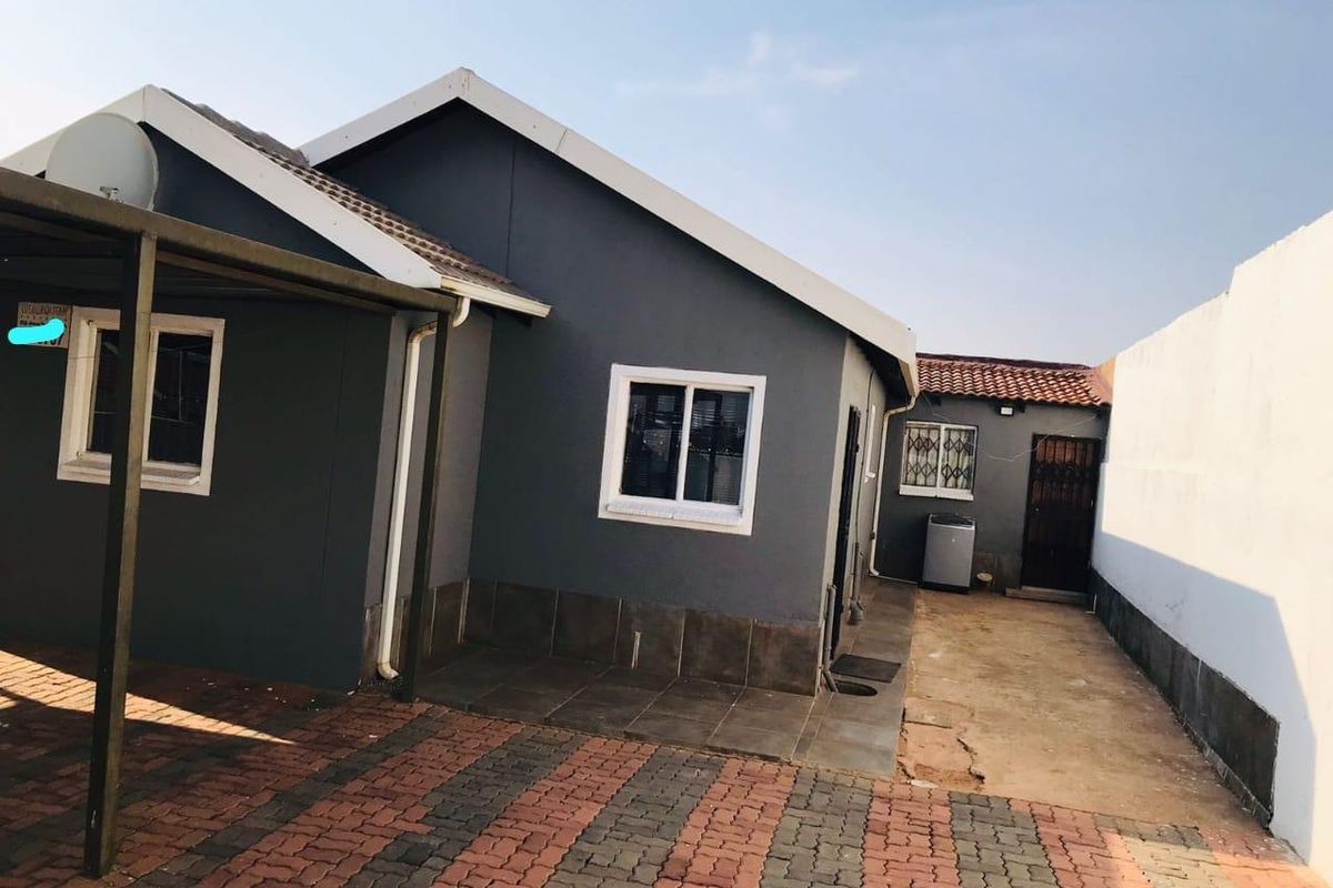 Rear exterior view of the property featuring a paved driveway, tiled patio area, and secure access gate.