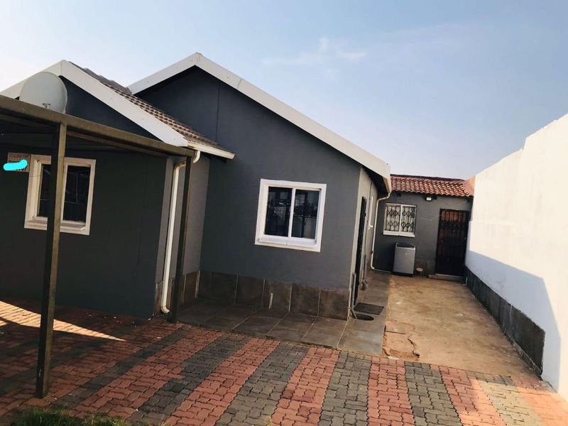 Rear exterior view of the property featuring a paved driveway, tiled patio area, and secure access gate.