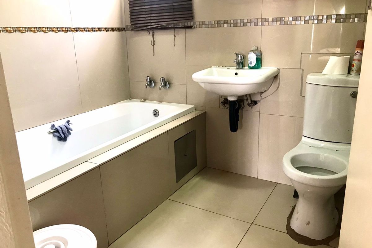A functional bathroom featuring a built-in bathtub, wall-mounted basin, and toilet with neutral floor-to-ceiling wall tiles.
