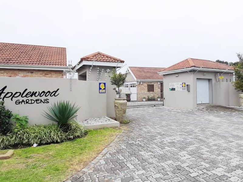 Front entrance view of Applewood Gardens townhouse complex, featuring a paved driveway, secure gated access, and perimeter wall with electric fencing.
