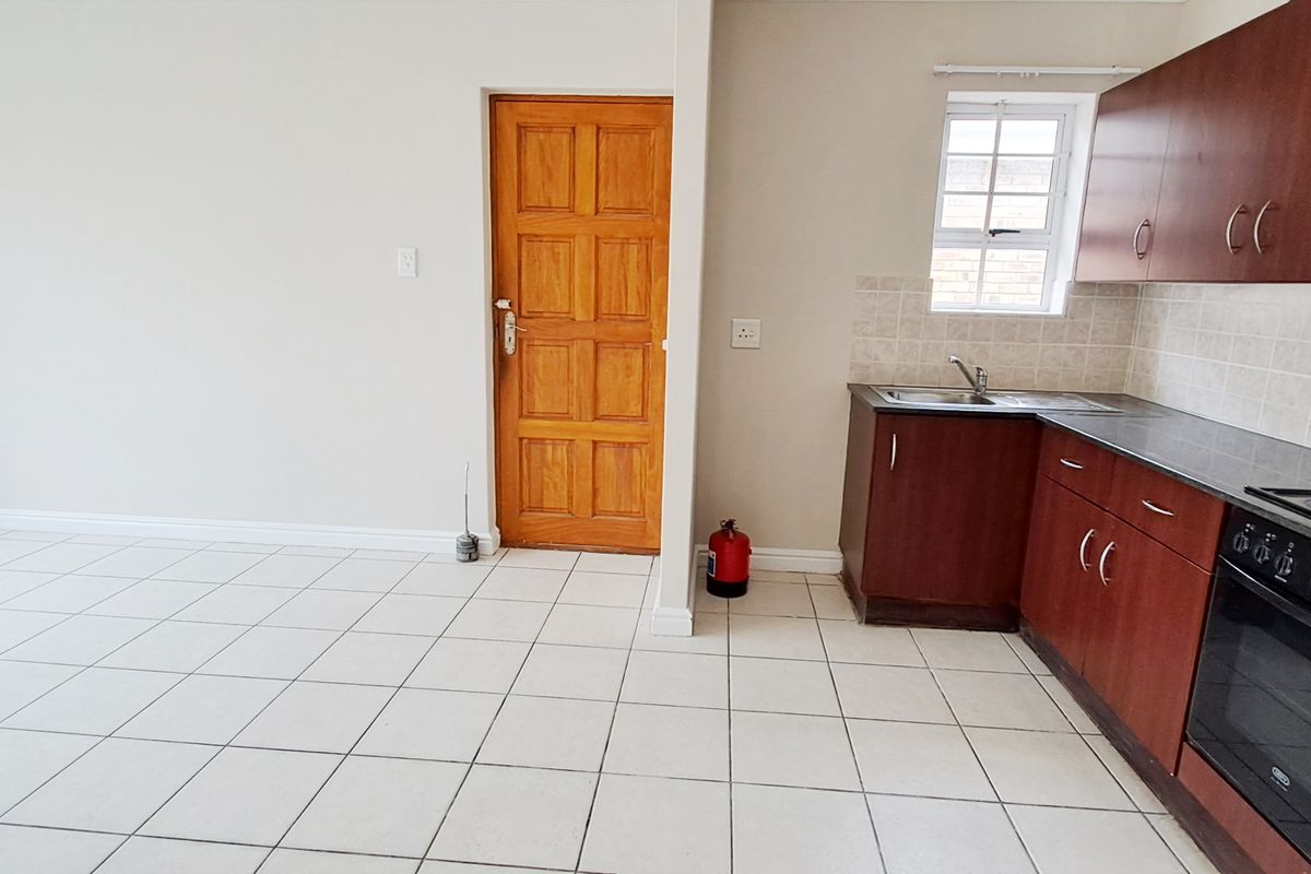 Open-plan living area featuring tiled floors and a functional kitchen with built-in cabinetry, oven, extractor fan, and tiled backsplash.