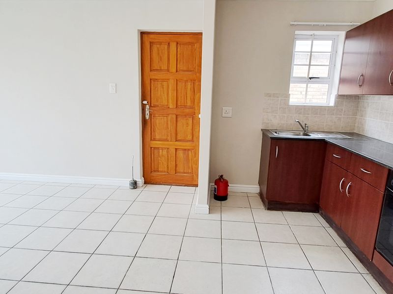 Open-plan living area featuring tiled floors and a functional kitchen with built-in cabinetry, oven, extractor fan, and tiled backsplash.