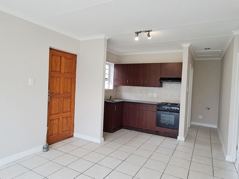 Open-plan kitchen area featuring dark wood cabinetry, tiled flooring, and a built-in stove with extractor fan, leading to an entrance door.