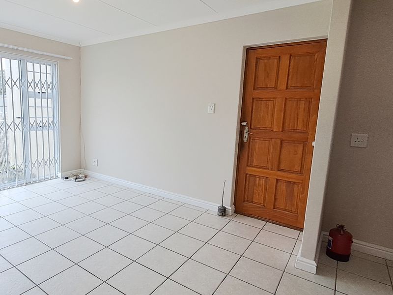 An open-plan living area featuring neutral tiled flooring, a wooden entrance door, and a sliding glass door with a security gate leading outdoors.