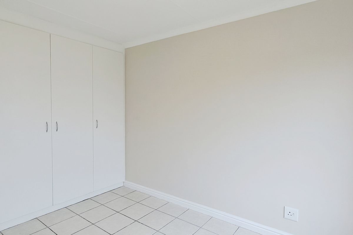 A clean, empty bedroom featuring neutral walls, tiled flooring, and built-in cupboards, offering a versatile space ready for personalization.