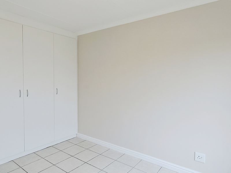 A clean, empty bedroom featuring neutral walls, tiled flooring, and built-in cupboards, offering a versatile space ready for personalization.