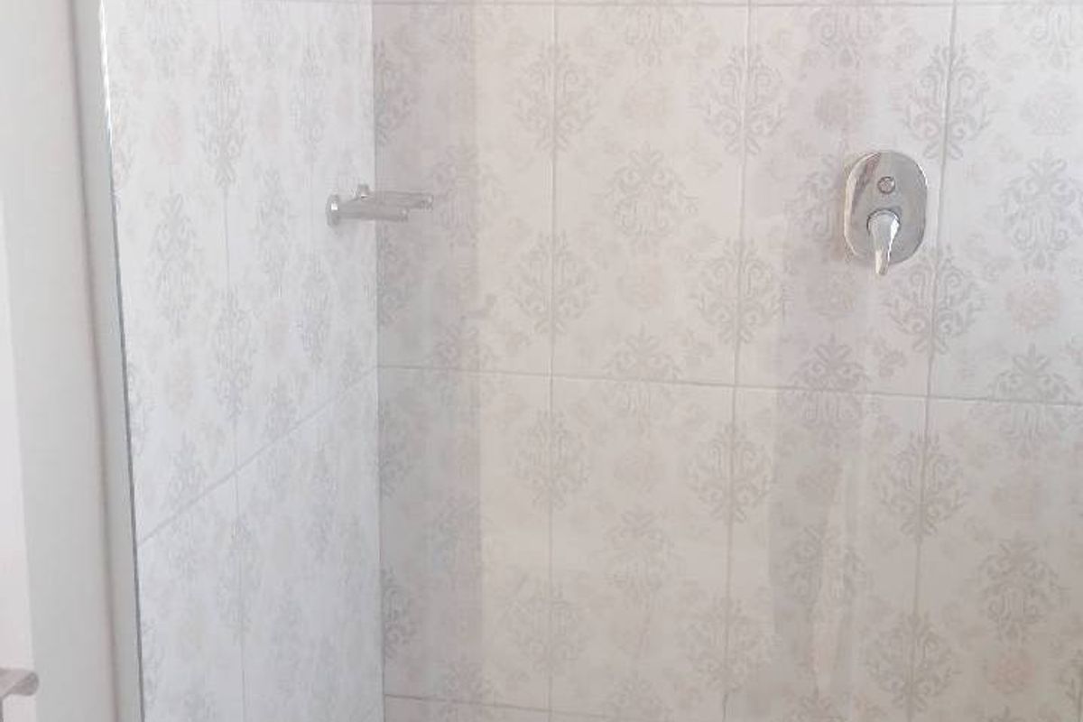 A clean, modern shower enclosure featuring patterned wall tiles, a built-in shower mixer, and a white shower tray.