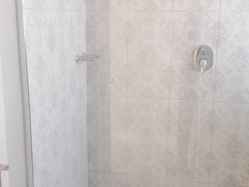 A clean, modern shower enclosure featuring patterned wall tiles, a built-in shower mixer, and a white shower tray.