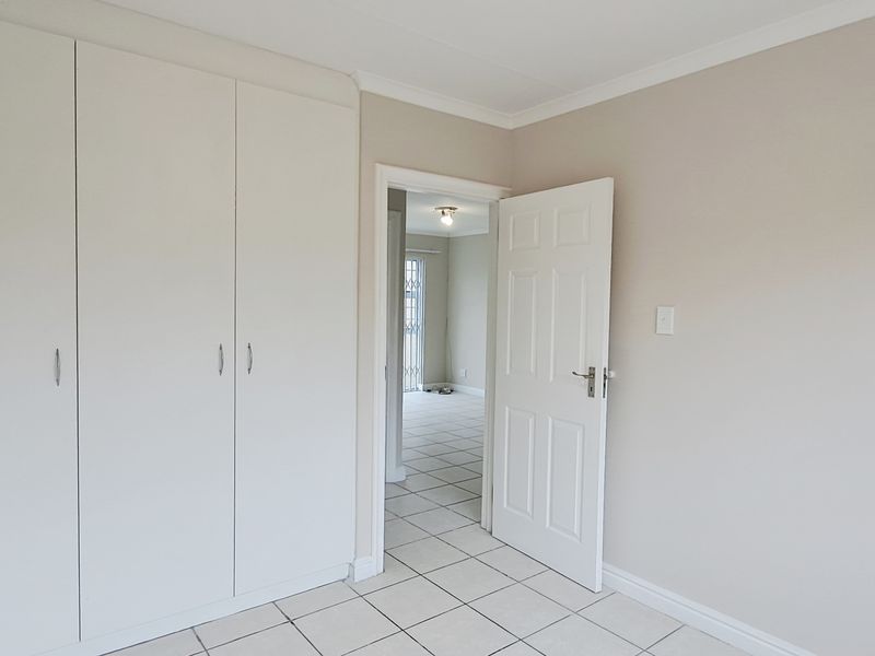 A clean, empty bedroom featuring neutral wall tones, tiled flooring, and ample built-in cupboard storage space.