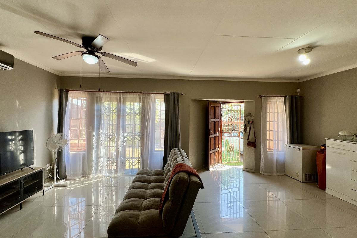 Spacious living room featuring large format floor tiles, a ceiling fan, and direct access to the exterior through a security gate.