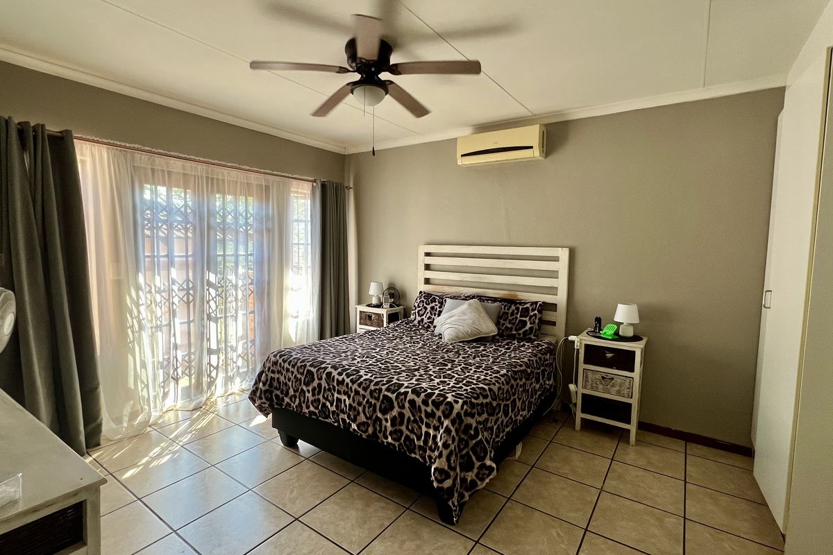 A bedroom featuring tiled flooring, a ceiling fan, and a wall-mounted air conditioning unit, with sliding glass doors providing access to the exterior.