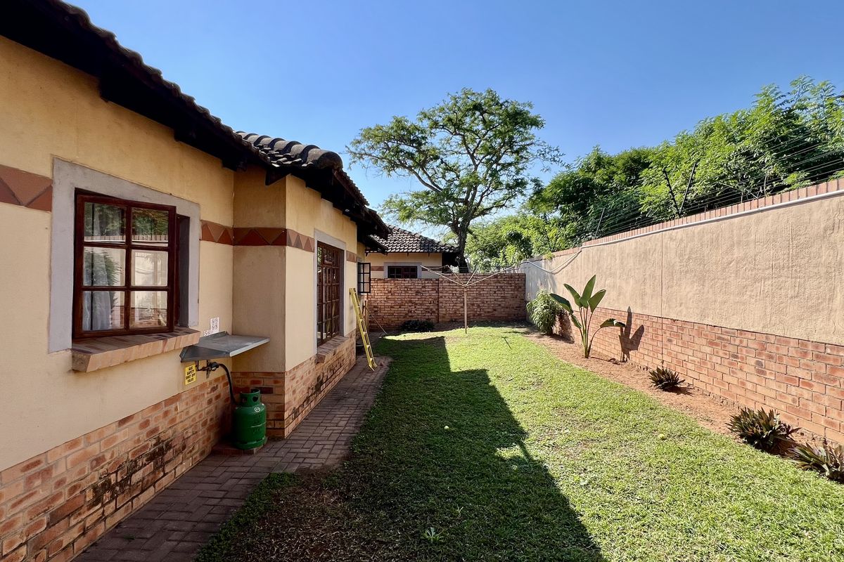 A view of the rear garden featuring a paved walkway, brick boundary walls, and a lawn area adjacent to the house exterior.