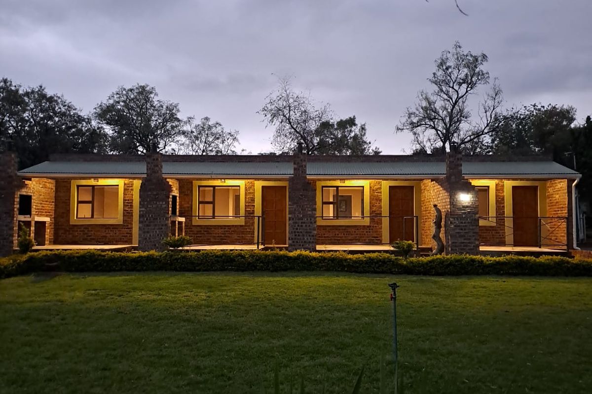 Exterior view of a single-story apartment block featuring brick facade, covered patio walkway, and integrated outdoor lighting at dusk.