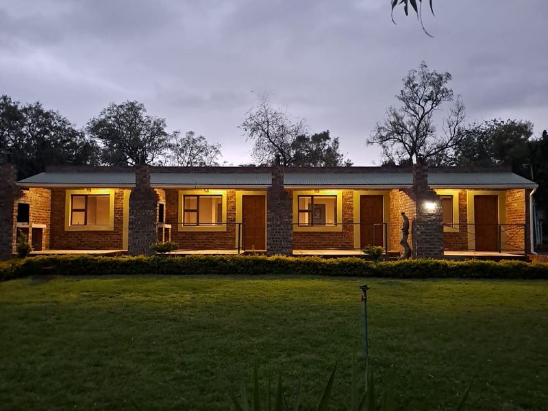 Exterior view of a single-story apartment block featuring brick facade, covered patio walkway, and integrated outdoor lighting at dusk.