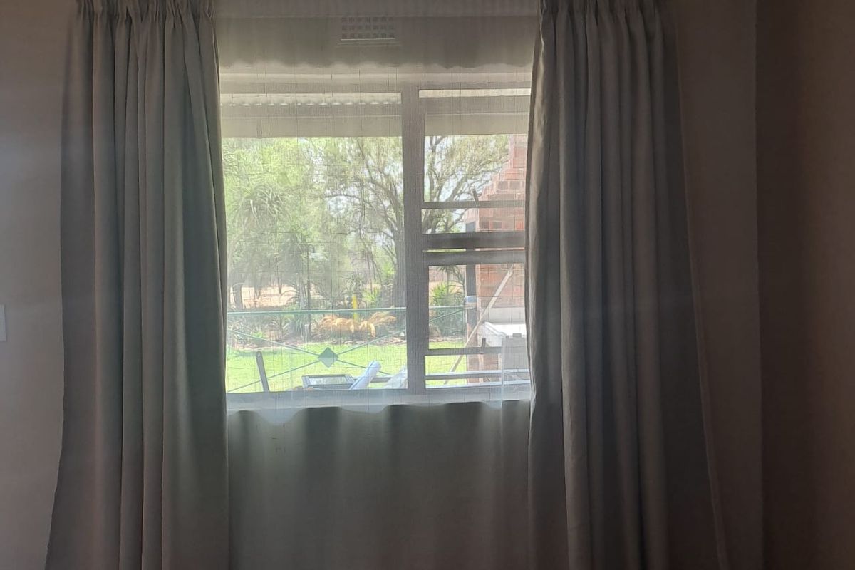 A bedroom interior featuring a window with curtains, providing a view of the outdoor garden area.