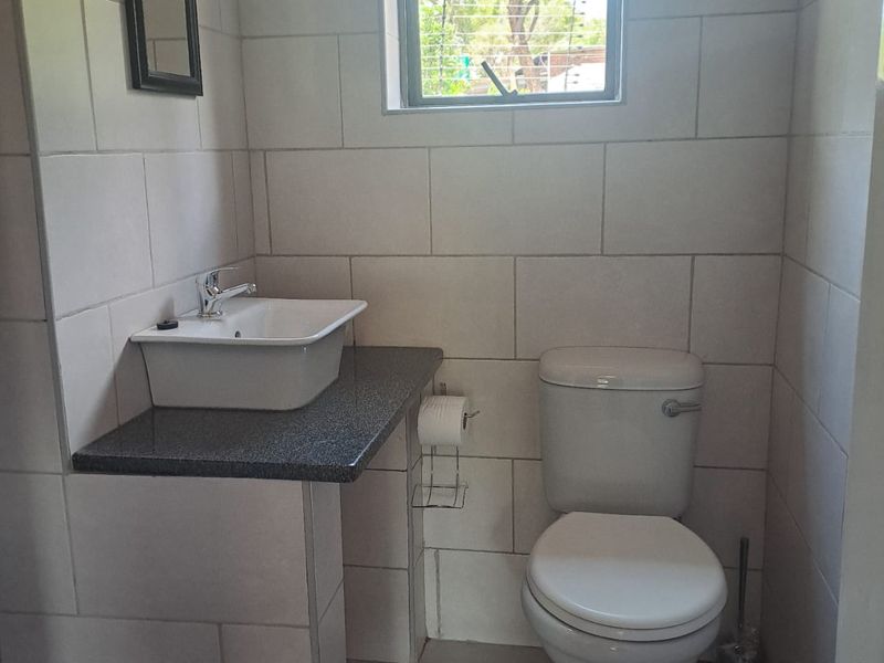 A compact bathroom featuring a wall-mounted basin on a stone-look vanity top, a standard toilet, and full-height wall tiling.