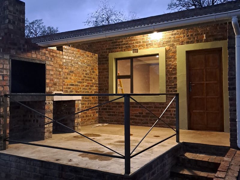 A rustic outdoor patio area featuring a built-in brick braai, metal railing, and direct access to the apartment interior.