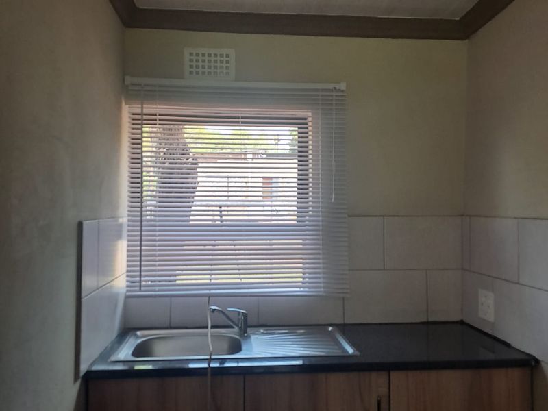 A functional kitchen area featuring a stainless steel sink, dark countertop, and wooden cabinetry with tiled splashback.
