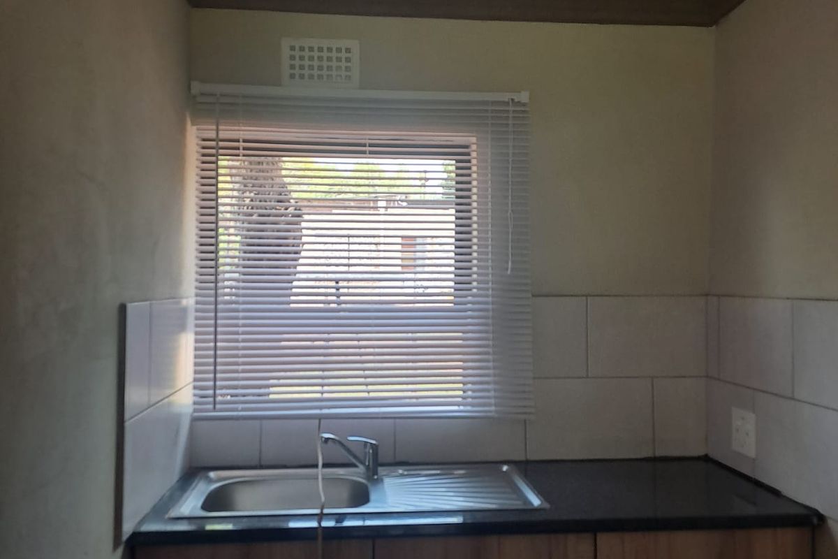 A functional kitchen area featuring a stainless steel sink, dark countertop, and wooden cabinetry with tiled splashback.