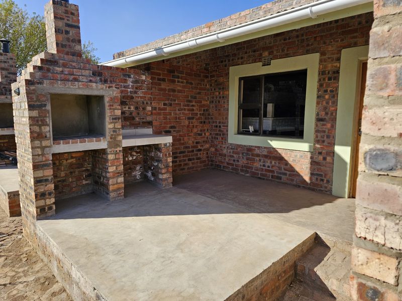 A rustic outdoor patio area featuring a built-in brick braai and chimney, set against a face-brick exterior wall with a window.