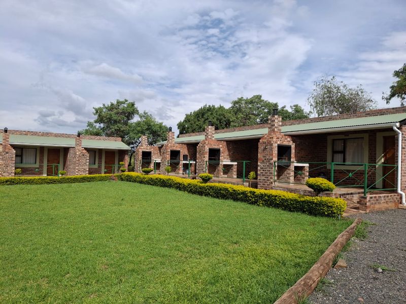 Exterior view of a row of brick apartment units featuring individual built-in braai areas and a shared landscaped garden space.