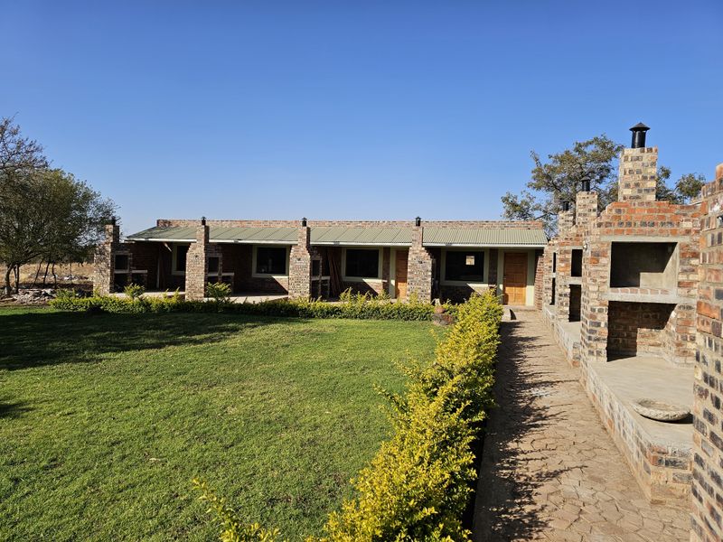 Exterior view of a brick-built apartment building featuring a covered patio area, outdoor brick braai facilities, and a well-maintained garden.