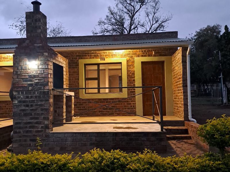A charming exterior view of a brick-built apartment featuring a covered patio area with a built-in fireplace and outdoor lighting.
