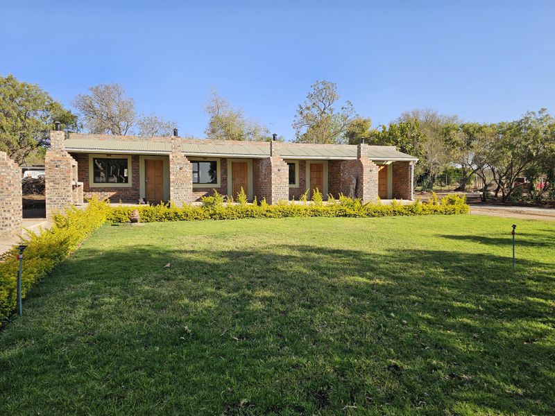A well-maintained single-story brick apartment building featuring multiple entrance doors, metal roofing, and a spacious front lawn with established landscaping.