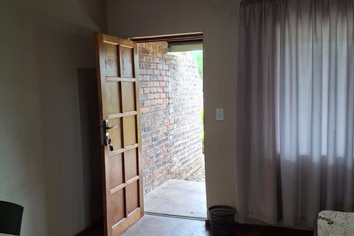 Interior view of a room featuring a wooden door leading to an exterior brick-walled patio area with concrete flooring.