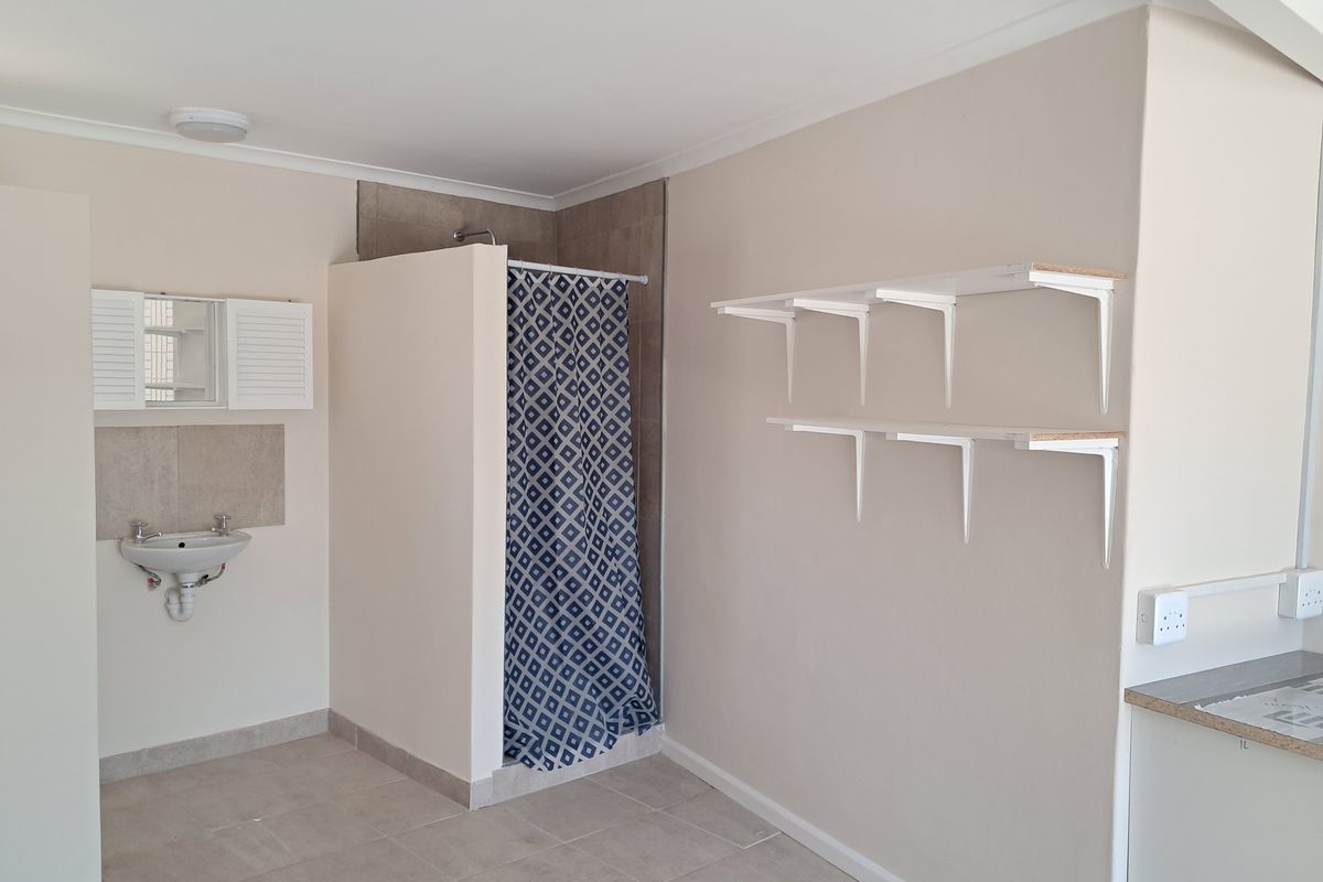 A functional bathroom featuring a wall-mounted basin, a shower enclosure with a curtain, and wall-mounted shelving units.