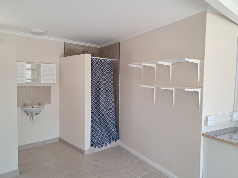 A functional bathroom featuring a wall-mounted basin, a shower enclosure with a curtain, and wall-mounted shelving units.
