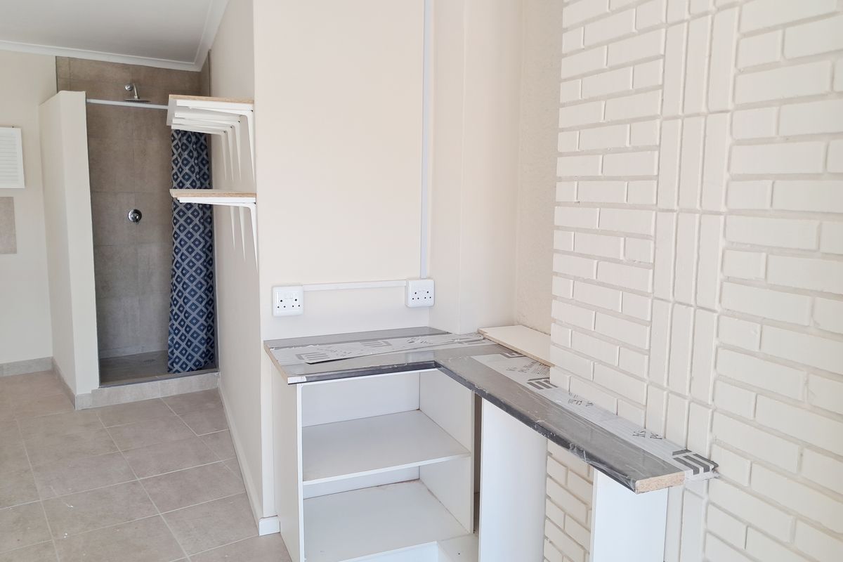 A functional bathroom space featuring a walk-in shower, tiled flooring, and a built-in vanity area with an exposed brick feature wall.