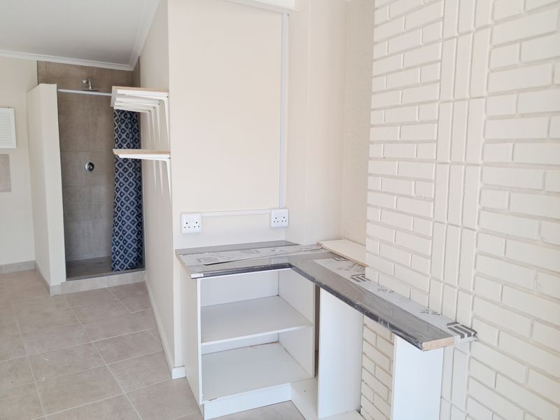 A functional bathroom space featuring a walk-in shower, tiled flooring, and a built-in vanity area with an exposed brick feature wall.