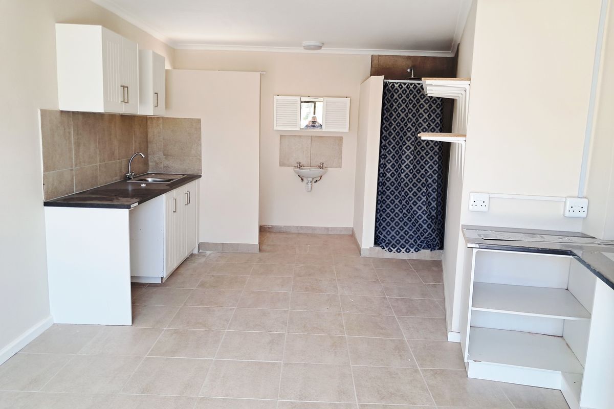 Open plan studio apartment featuring a basic kitchenette with sink, tiled flooring, and a separate shower area with wall-mounted basin.