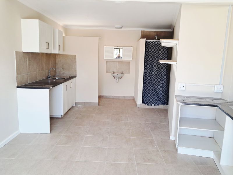 Open plan studio apartment featuring a basic kitchenette with sink, tiled flooring, and a separate shower area with wall-mounted basin.