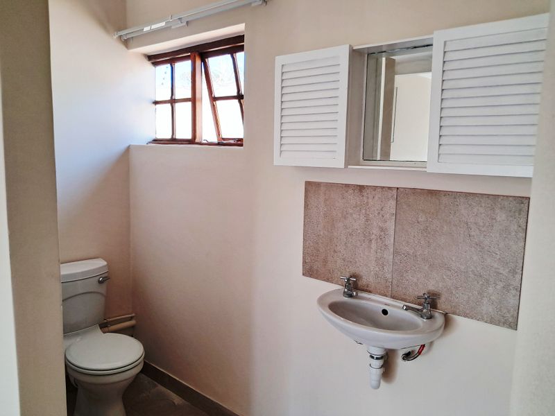 A functional bathroom featuring a wall-mounted basin with tiled splashback, medicine cabinet, and a standard toilet under a timber-framed window.
