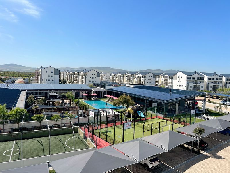 Aerial view of the apartment complex featuring a swimming pool, padel and soccer courts, and covered parking facilities.