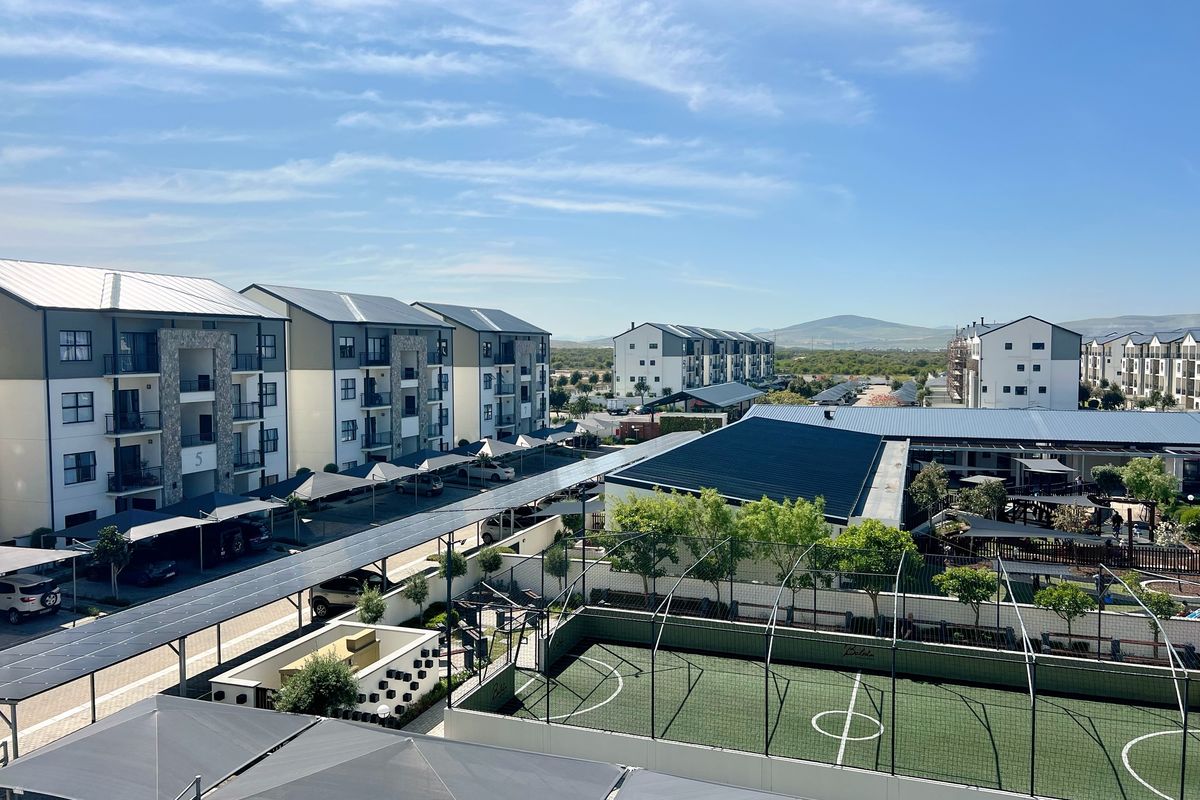 Aerial view of a modern apartment complex featuring paved parking with solar panel carports, a fenced sports court, and well-maintained landscaped grounds.
