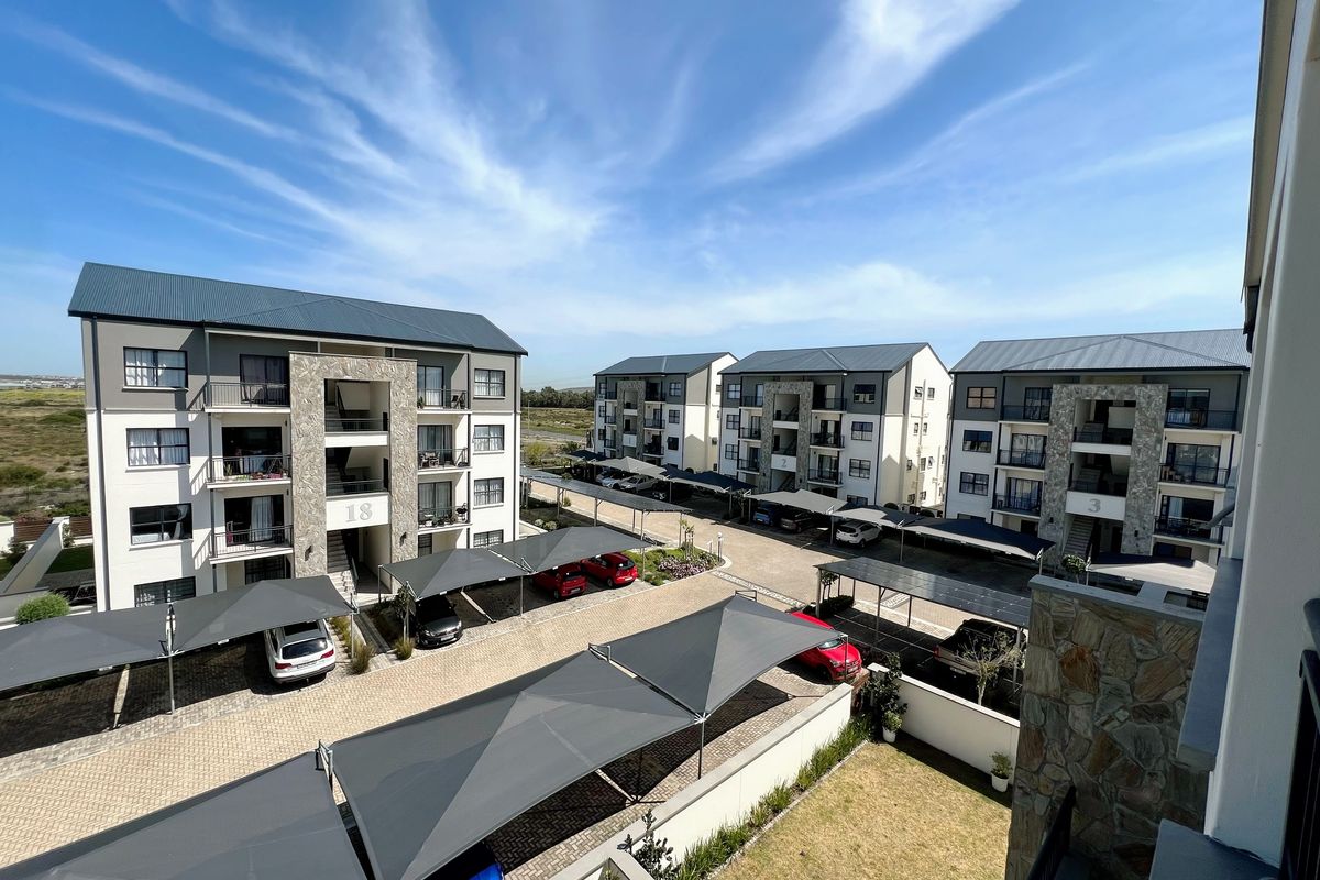 Elevated view of an apartment complex featuring multiple residential blocks, paved parking areas with shade-cloth carports, and stone-clad architectural detailing.