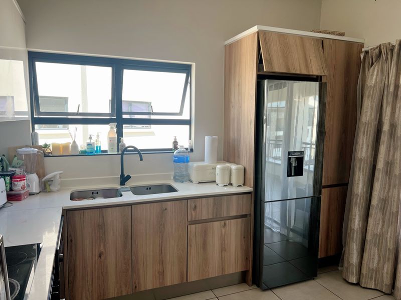 Modern kitchen featuring wood-look cabinetry, stone countertops, a double sink with a black mixer tap, and integrated fridge housing.
