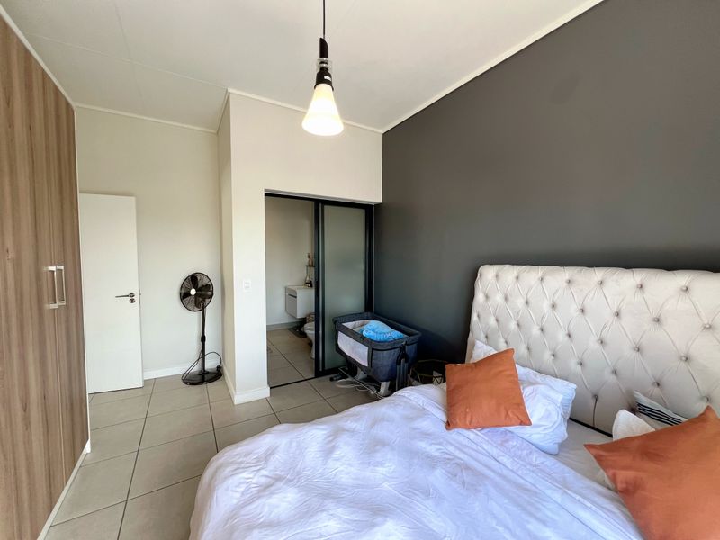 A modern bedroom featuring tiled floors, a large built-in wardrobe, and direct access to an en-suite bathroom through a sliding door.