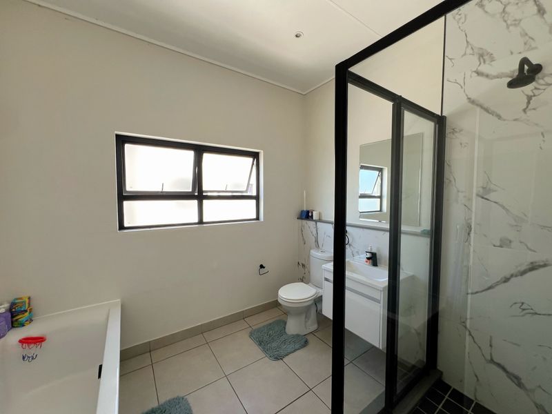 Modern bathroom featuring a glass-enclosed shower with marble-look tiling, a vanity unit, toilet, and a bathtub, finished with neutral floor tiles.