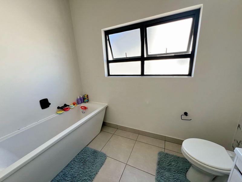 A clean, modern bathroom featuring a white bathtub, a toilet, and contemporary black fixtures, complemented by large neutral floor tiles and a window.