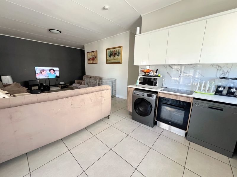 Open-plan living area featuring a modern kitchen with white cabinetry, marble-look splashback, integrated appliances, and neutral tiled flooring throughout.