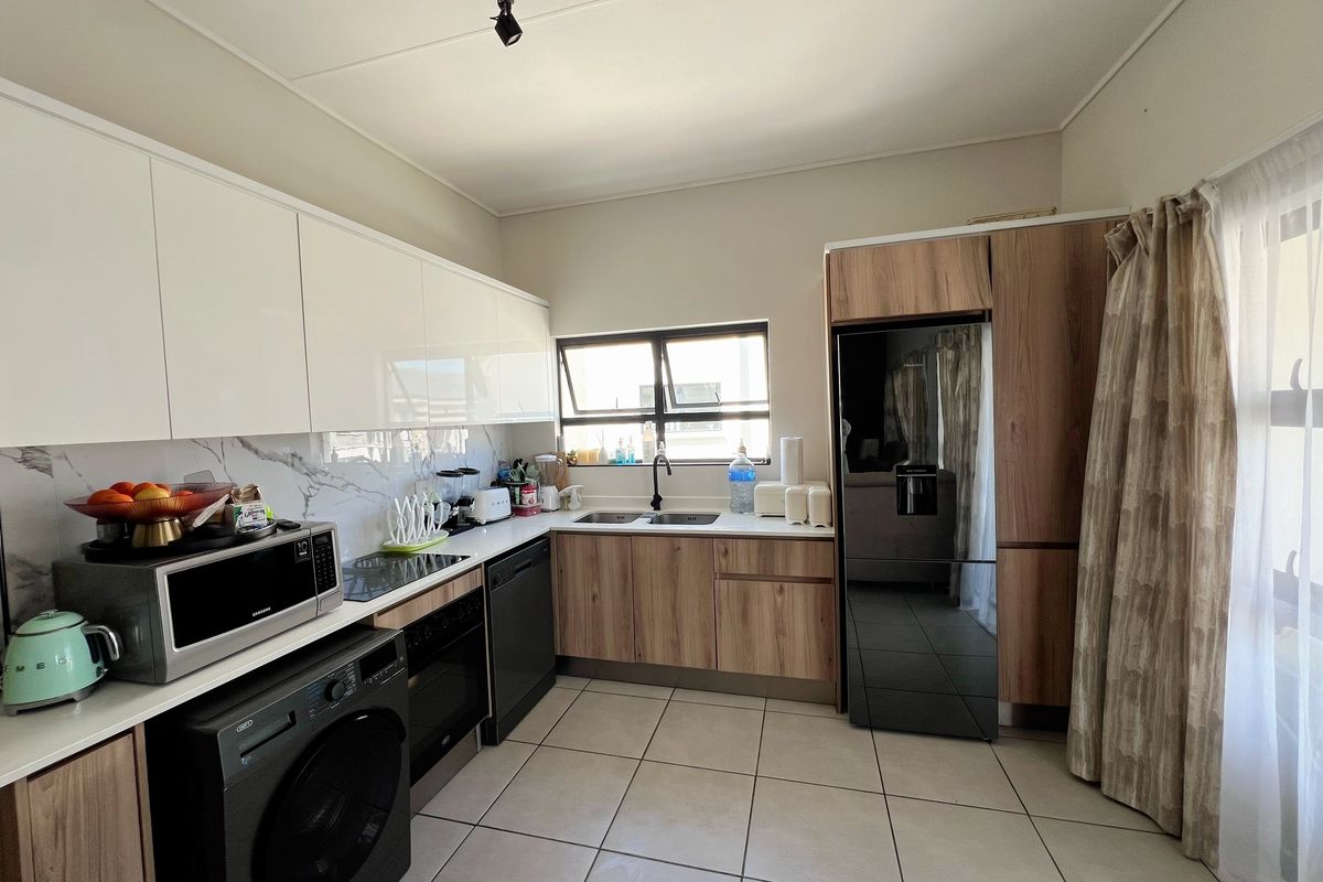 Modern kitchen featuring high-gloss white upper cabinets, wood-grain lower cabinetry, marble-look splashback, and integrated appliances with tiled flooring.