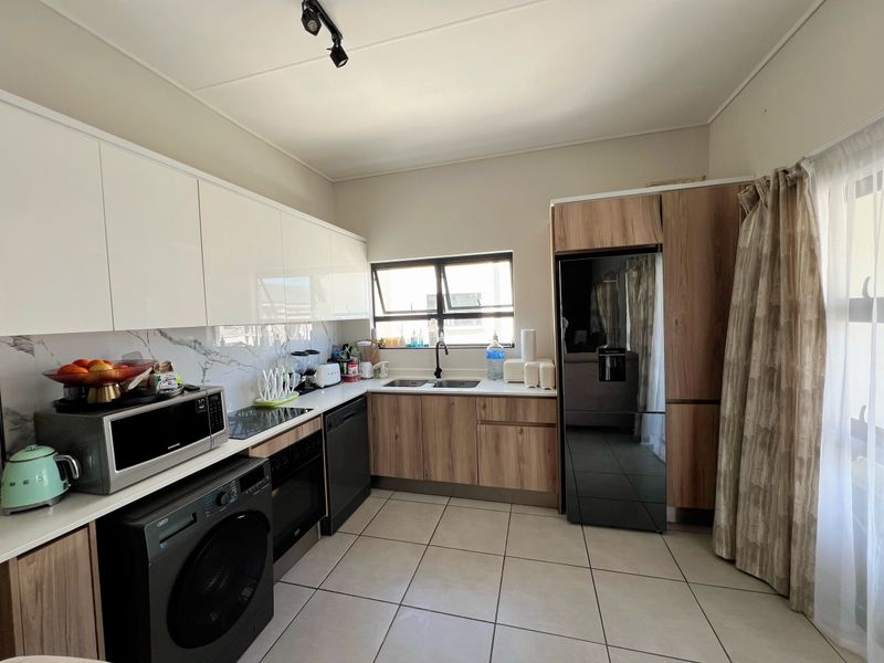 Modern kitchen featuring high-gloss white upper cabinets, wood-grain lower cabinetry, marble-look splashback, and integrated appliances with tiled flooring.