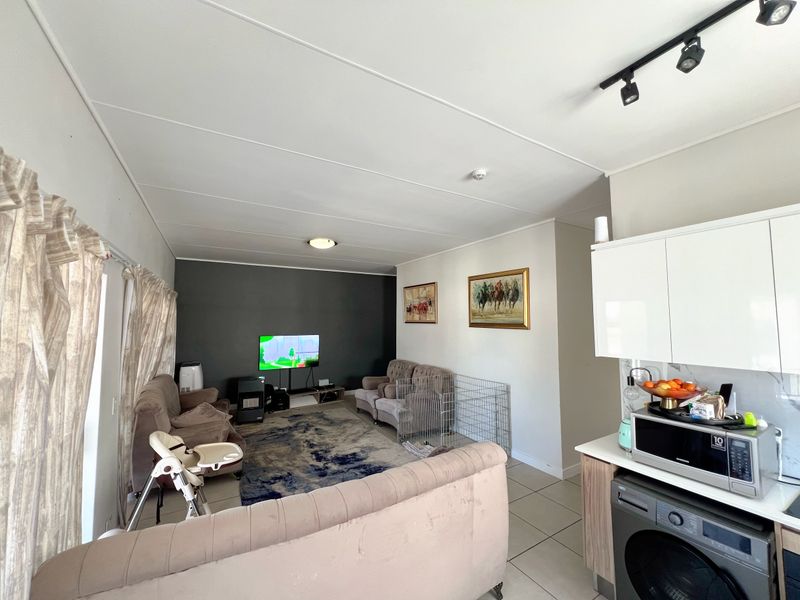 An open-plan living and kitchen area featuring tiled flooring, track lighting, and modern white kitchen cabinetry.